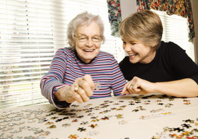 Elderly woman and a younger woman work on a jigsaw puzzle. Horizontal shot.